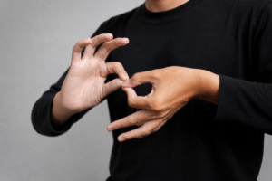A person wearing a black shirt using both hands to form the ASL sign for 'interpreter,' photographed from the chest down against gray background.